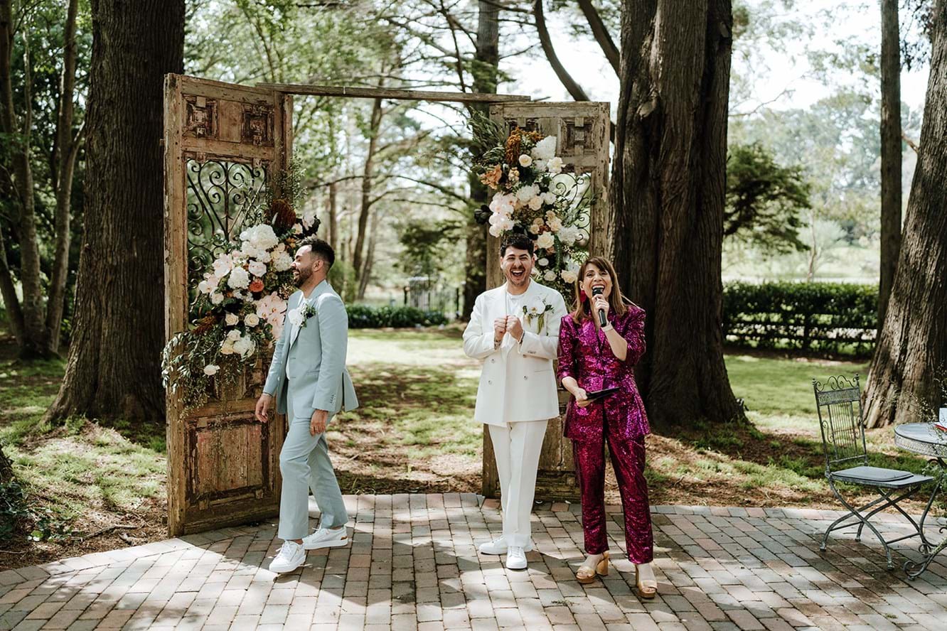 Two grooms laughing on their fun wedding day with their marriage celebrant and MC wearing pink sequins
